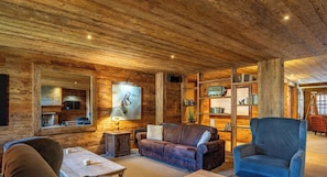Un intérieur rustique avec un plafond en bois, une cheminée, un canapé, un fauteuil et une bibliothèque.