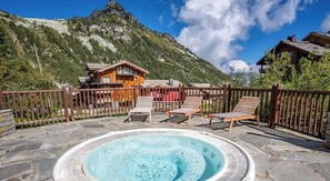 A hot tub surrounded by lounge chairs, with a mountain backdrop and wooden buildings. - Spacious 3 Bedroom Apartment - Arc 1950 - Refuge du Montagnard (Arc 1950)