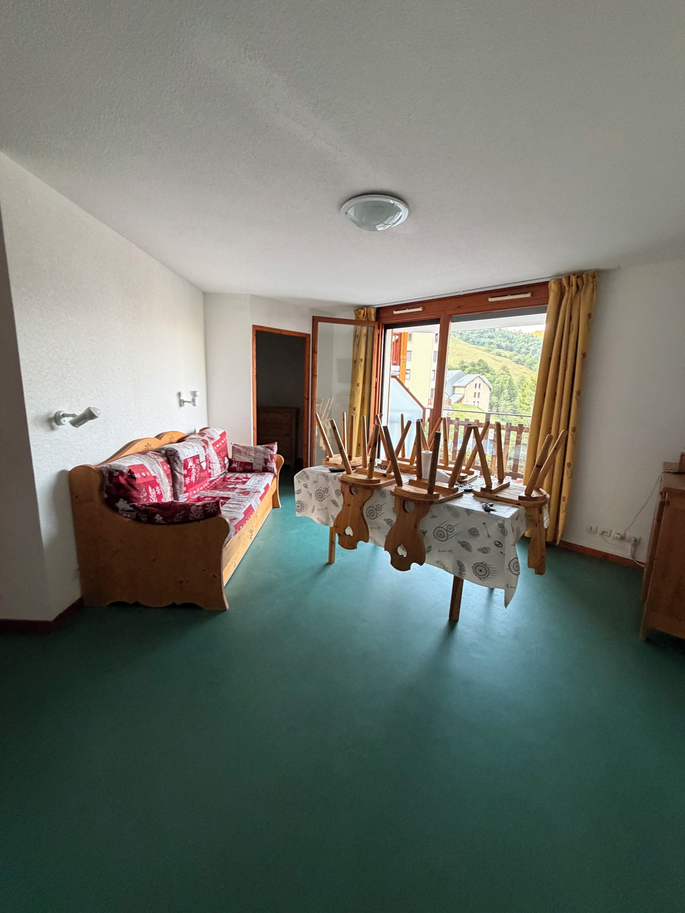 Ein Zimmer mit einem Bett, einem Tisch mit Tischdecke, einem Fenster mit Vorhängen und Blick auf Gebäude im Freien.