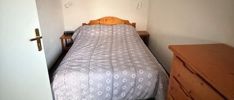 Una habitación pequeña con cama individual, cabecera de madera, alfombra verde y cómoda de madera.