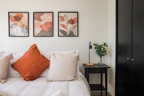 A bedroom with a bed, pillows, a nightstand with a lamp, a vase with flowers, and a wardrobe. - Modern Apartment in Ñuñoa for 3 Guest  (Ñuñoa)