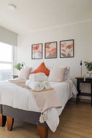 A neatly made bed with rolled towels, a bedside table with a lamp, and framed artwork on the wall. - Modern Apartment in Ñuñoa for 3 Guest  (Ñuñoa)