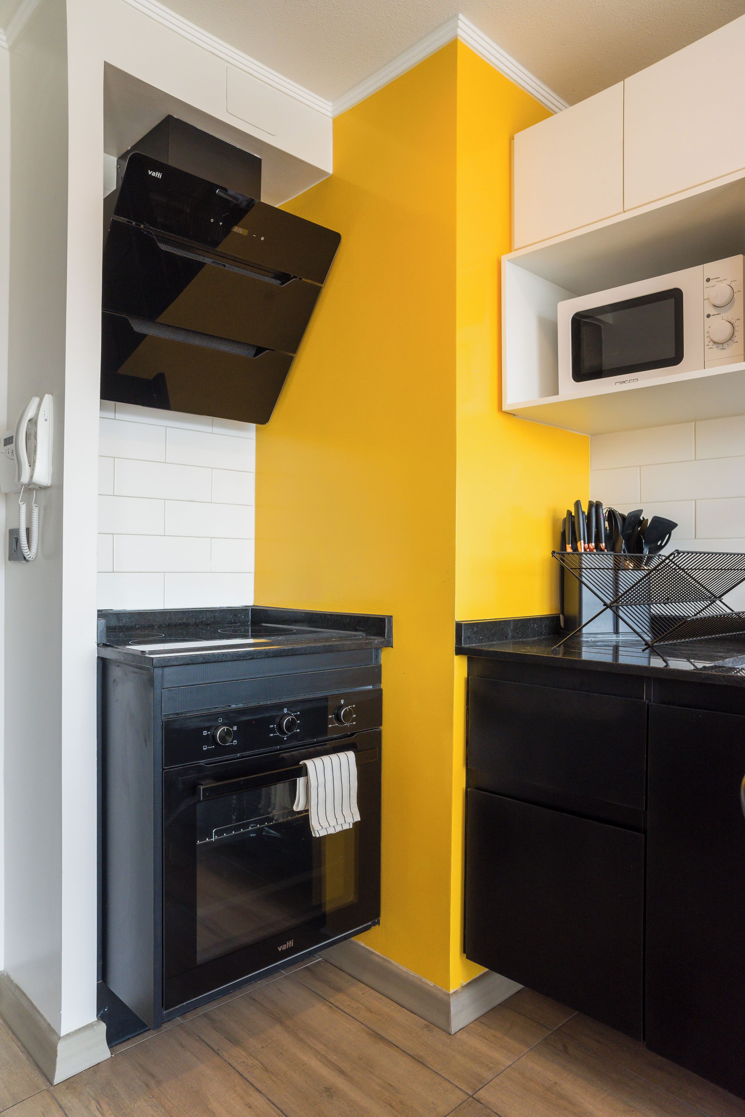 A kitchen with a black stove, oven, and microwave, a yellow accent wall, and white cabinetry.