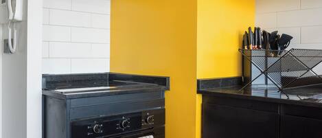 A kitchen with a black stove, oven, and microwave, a yellow accent wall, and white cabinetry.