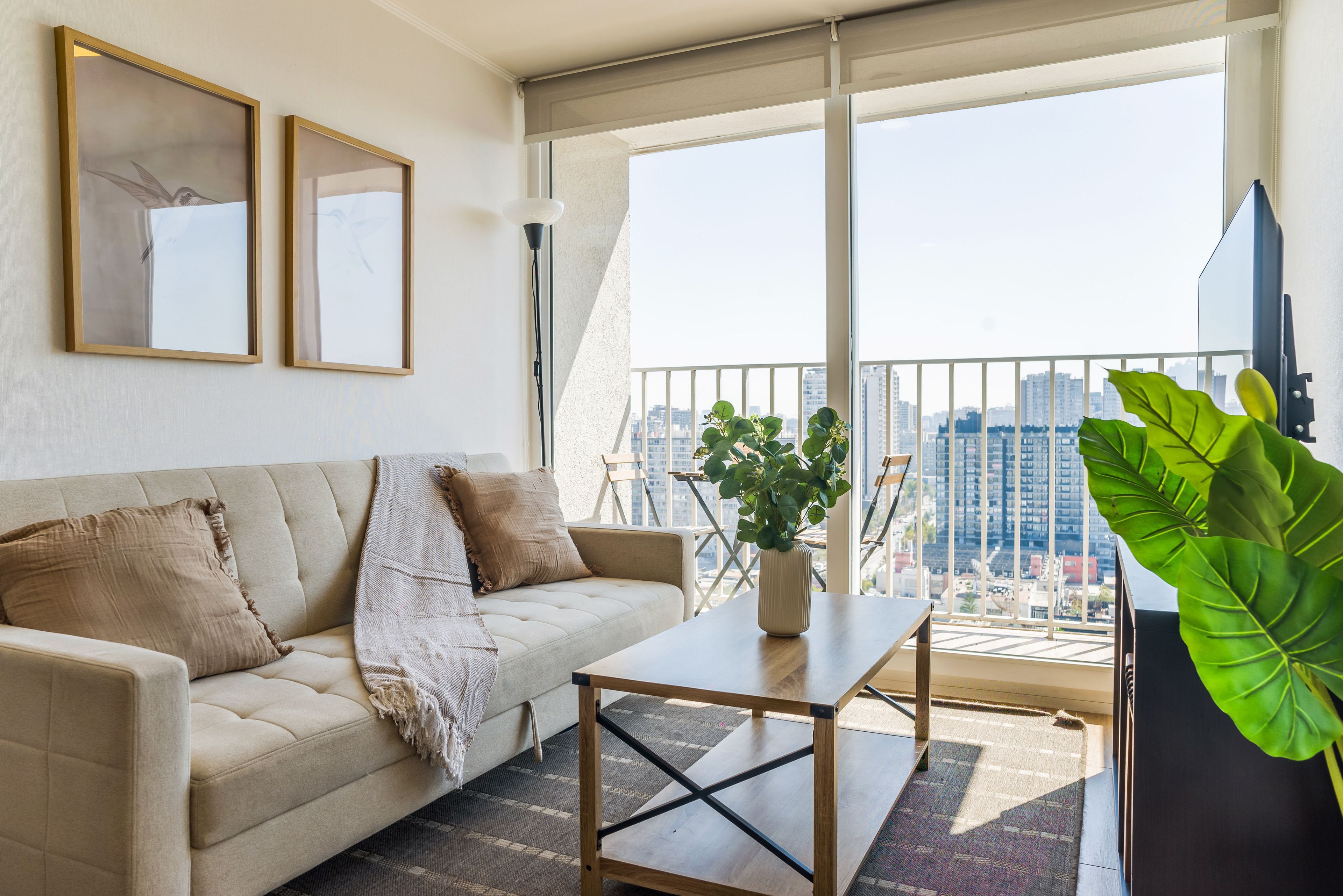 Una sala moderna con un sofá, una mesa de centro y vistas a un paisaje urbano a través de amplios ventanales.