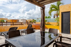 Eine Außenpatio mit einem Glastisch und Korbstühlen, umgeben von gelben Wänden und einer Holzpergola.
