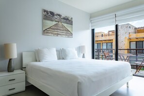 Ein modernes Hotelzimmer mit einem großen Bett, einem Nachttisch, einer Lampe und Blick auf die Stadt durch ein großes Fenster.