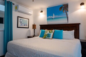 Ein Hotelzimmer mit einem Bett, einem Strandbild, einem Fenster mit Vorhängen und einer Klimaanlage.
