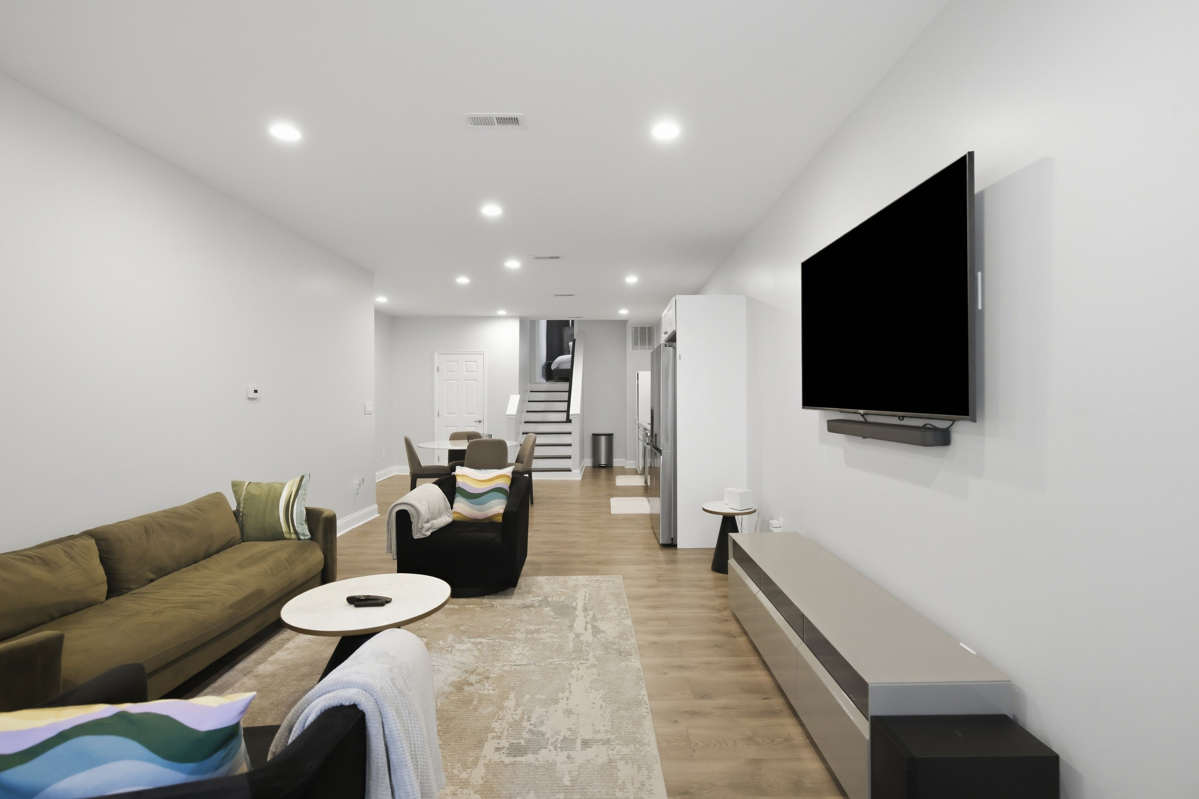 A modern living room with a sofa, a coffee table, a flat-screen TV mounted on the wall, and a staircase leading to another level.