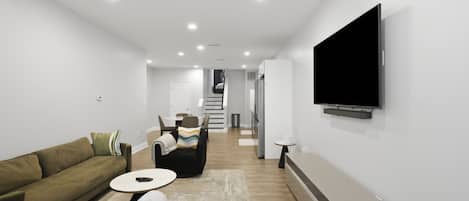 A modern living room with a sofa, a coffee table, a flat-screen TV mounted on the wall, and a staircase leading to another level.