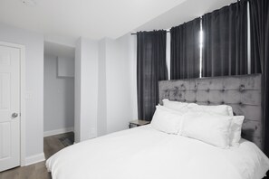 A bedroom with a large bed, a nightstand, a wall-mounted TV, and a door. - Stylish 1bd Urban Haven Near Inner Harbor 1 Bedroom Apts (Baltimore)