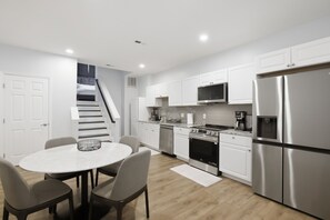 A modern kitchen with white cabinetry, stainless steel appliances, a dining area with a marble table, and a staircase leading to a loft bedroom. - Stylish 1bd Urban Haven Near Inner Harbor 1 Bedroom Apts (Baltimore)