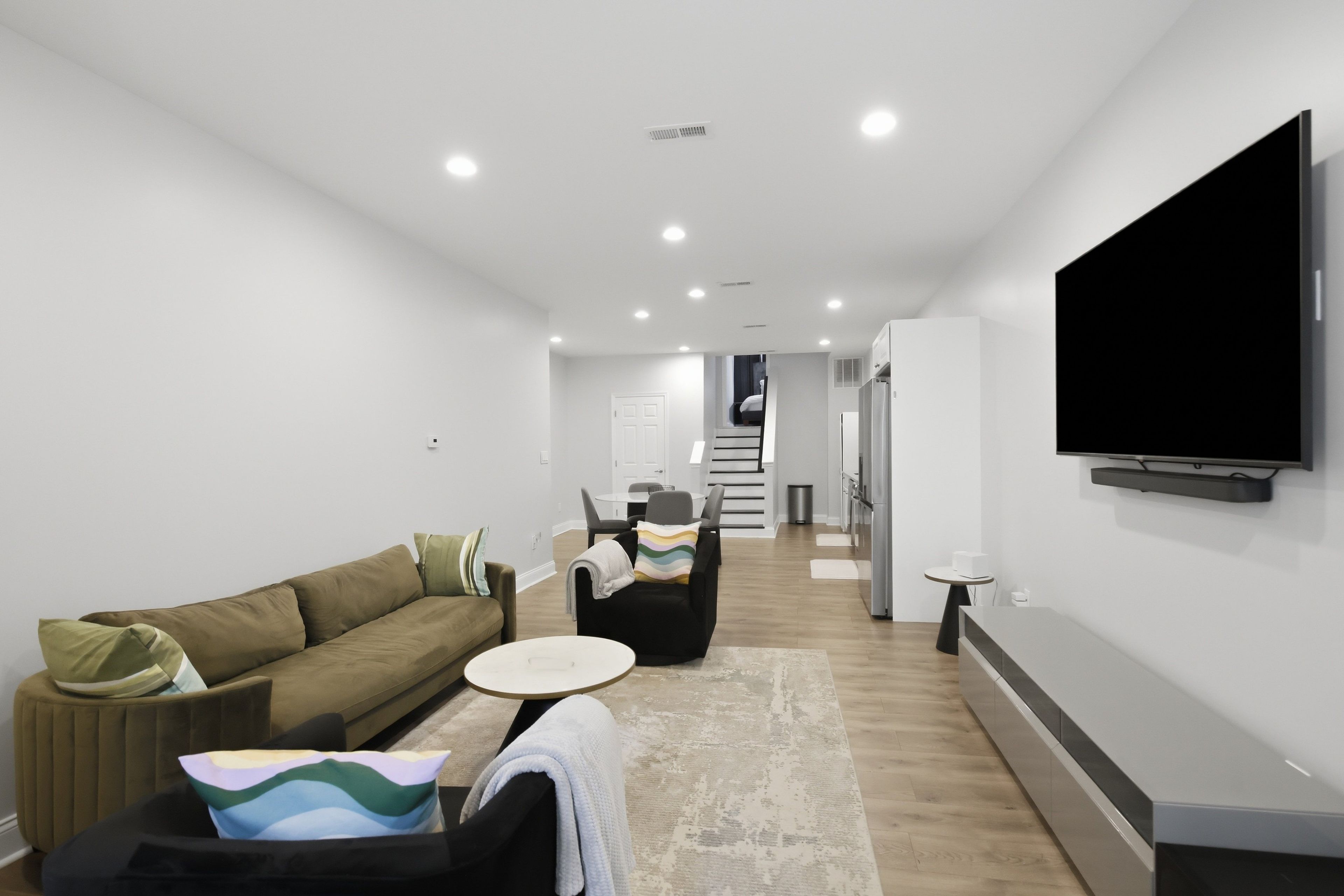 A modern living room with a sofa, armchairs, a coffee table, and a flat-screen TV mounted on the wall.