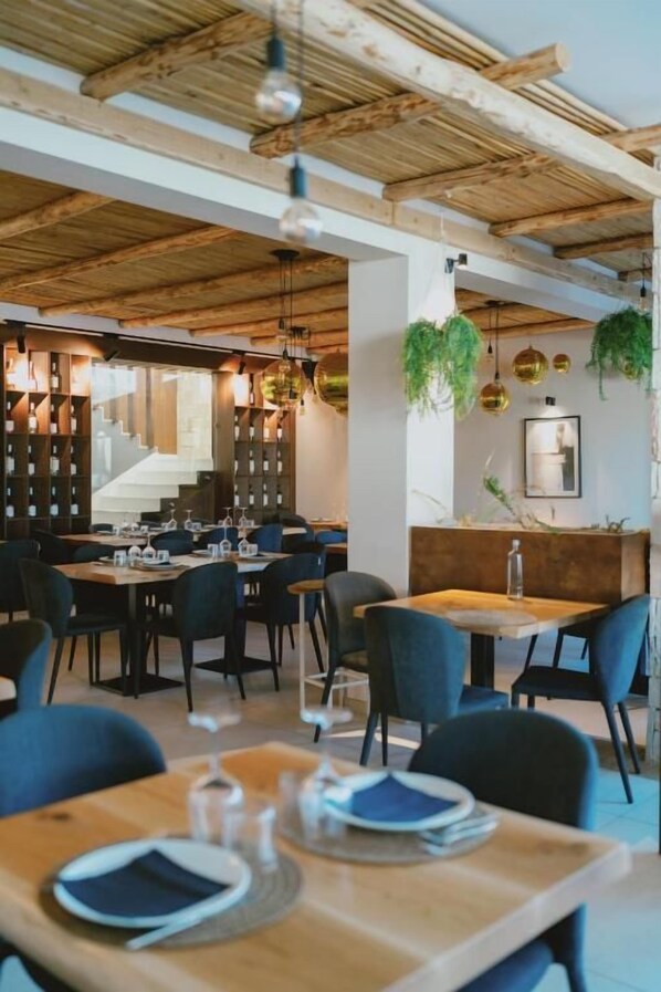 A restaurant interior with wooden beams, tables with blue chairs, and hanging plants.