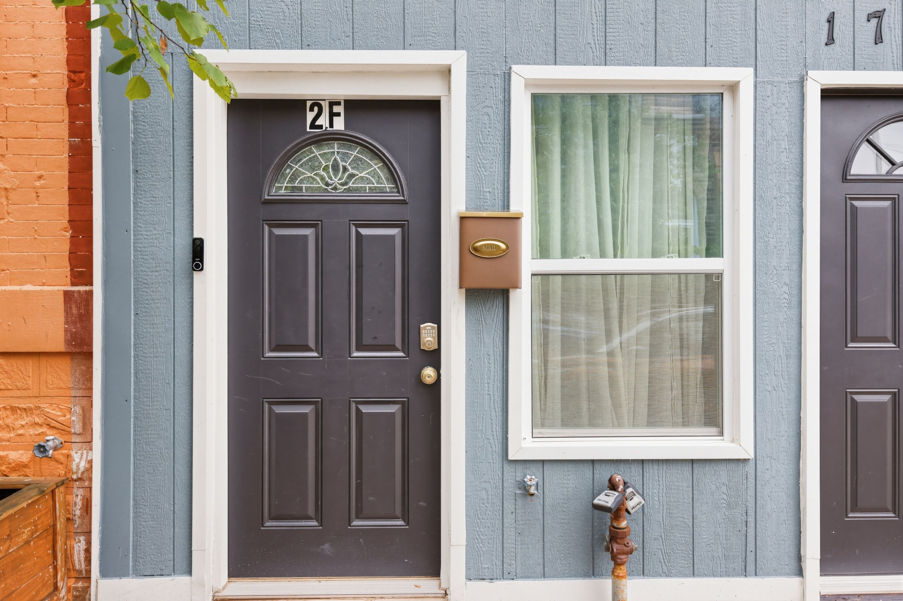 A dark-colored door with a number plate, a mail slot, and a window with a curtain.