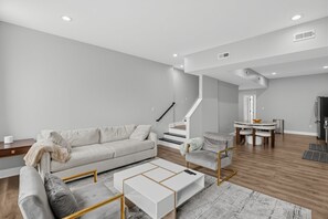 A modern living room with a sofa, coffee table, and a staircase leading to a dining area. - Expansive Urban Canvas In Baltimore 4 Bedroom Apts (Baltimore)