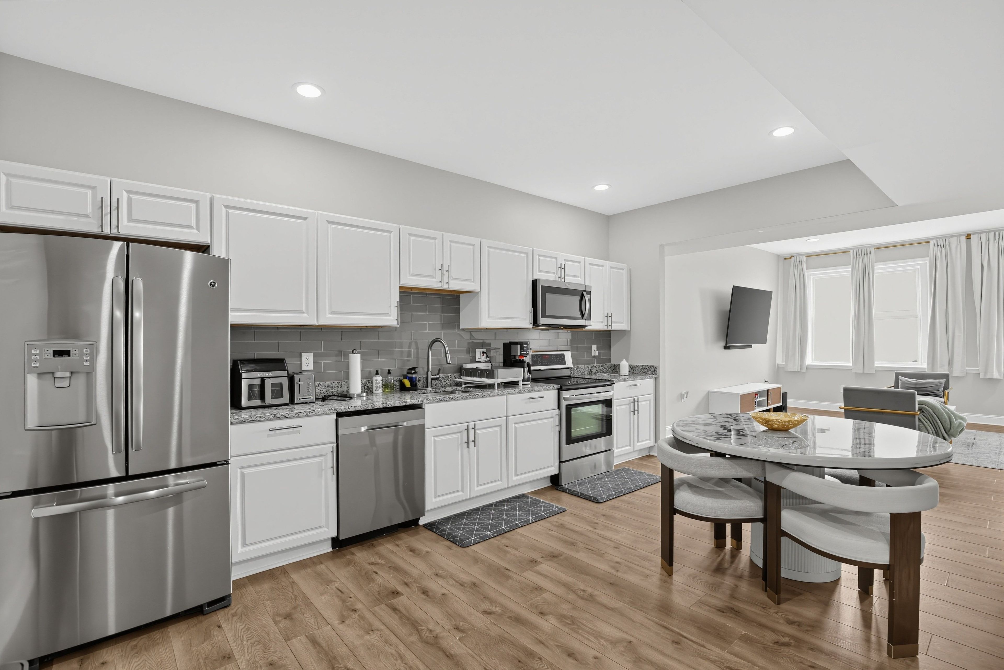 A modern kitchen with stainless steel appliances, white cabinetry, and a dining area with a round table and chairs.
