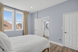 A bedroom with a bed, a window, a door, and a bathroom visible through an open door. - Expansive Urban Canvas In Baltimore 4 Bedroom Apts (Baltimore)
