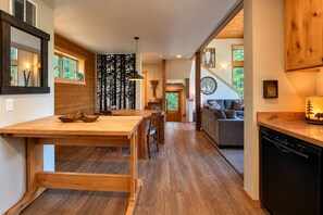 A modern kitchen with wooden flooring, a dining area with a large table and chairs, and a living room with a sofa and a lamp.