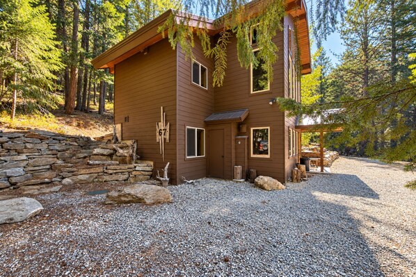 A cabin with a stone wall entrance, a gravel driveway, and a forested backdrop.