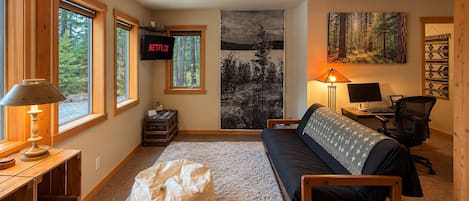 A cozy living room with a sofa, a bean bag, a desk with a computer, and a TV displaying 'NETFLIX'.