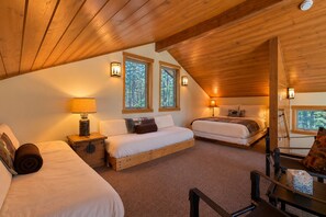 A cozy bedroom with two beds, a wooden ceiling, and windows with a forest view.