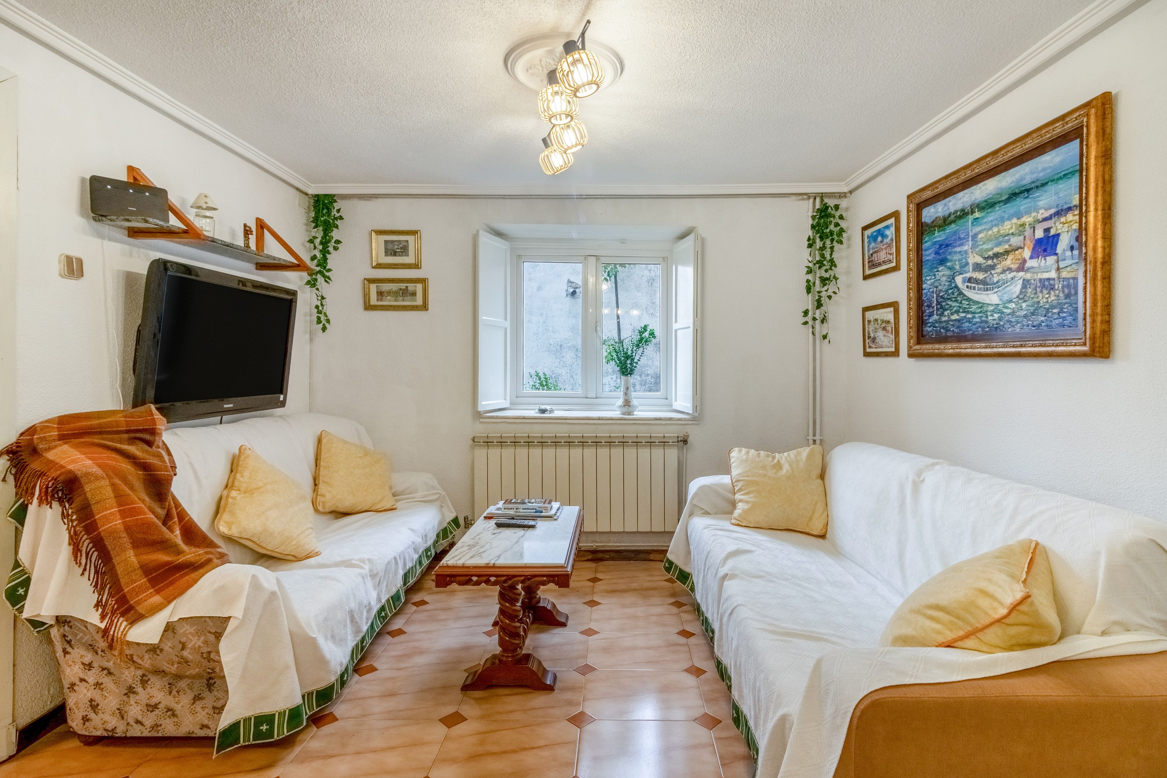 Una sala de estar con dos sofás blancos, una mesa de centro, un televisor y un ventanal con vistas a zonas verdes.