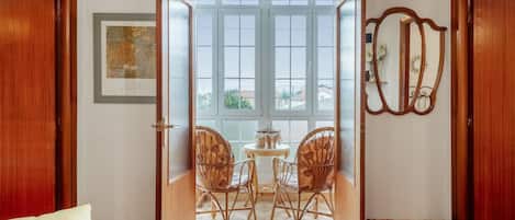 Una habitación con puerta de madera que da a un balcón con vistas, una pequeña mesa con sillas y un espejo en la pared.
