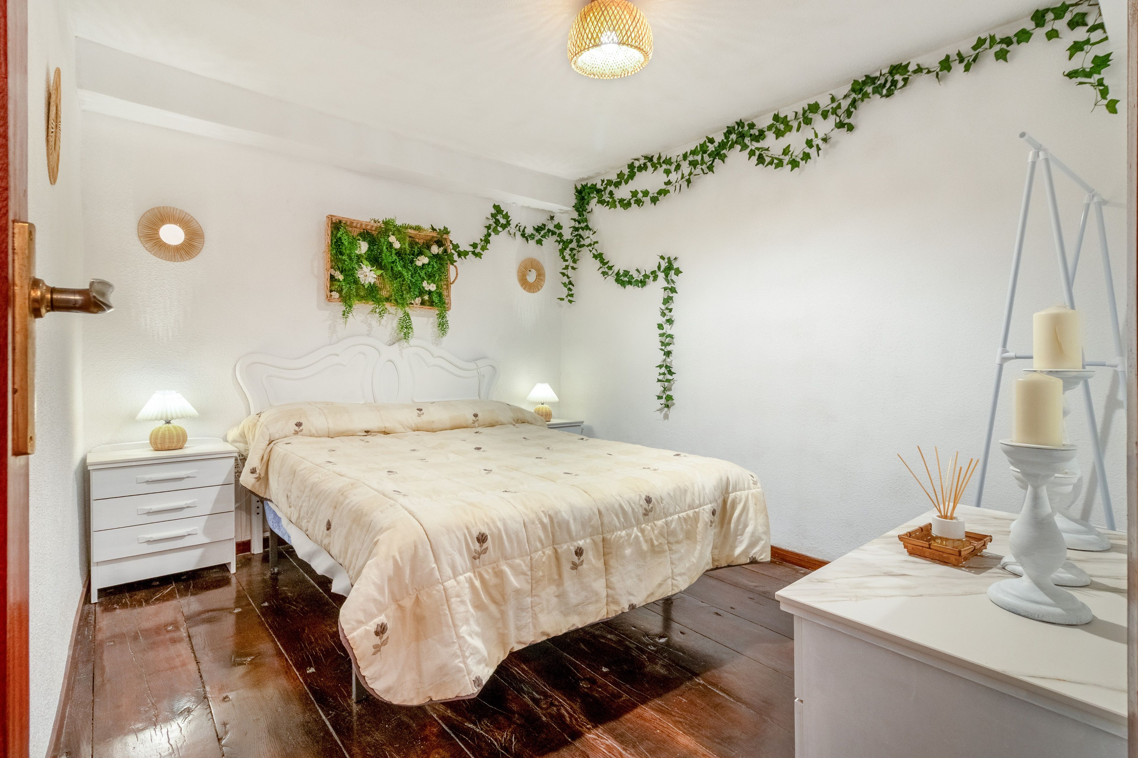 A bedroom with a bed, bedside tables, a lamp, a wall-mounted plant, and a mirror.