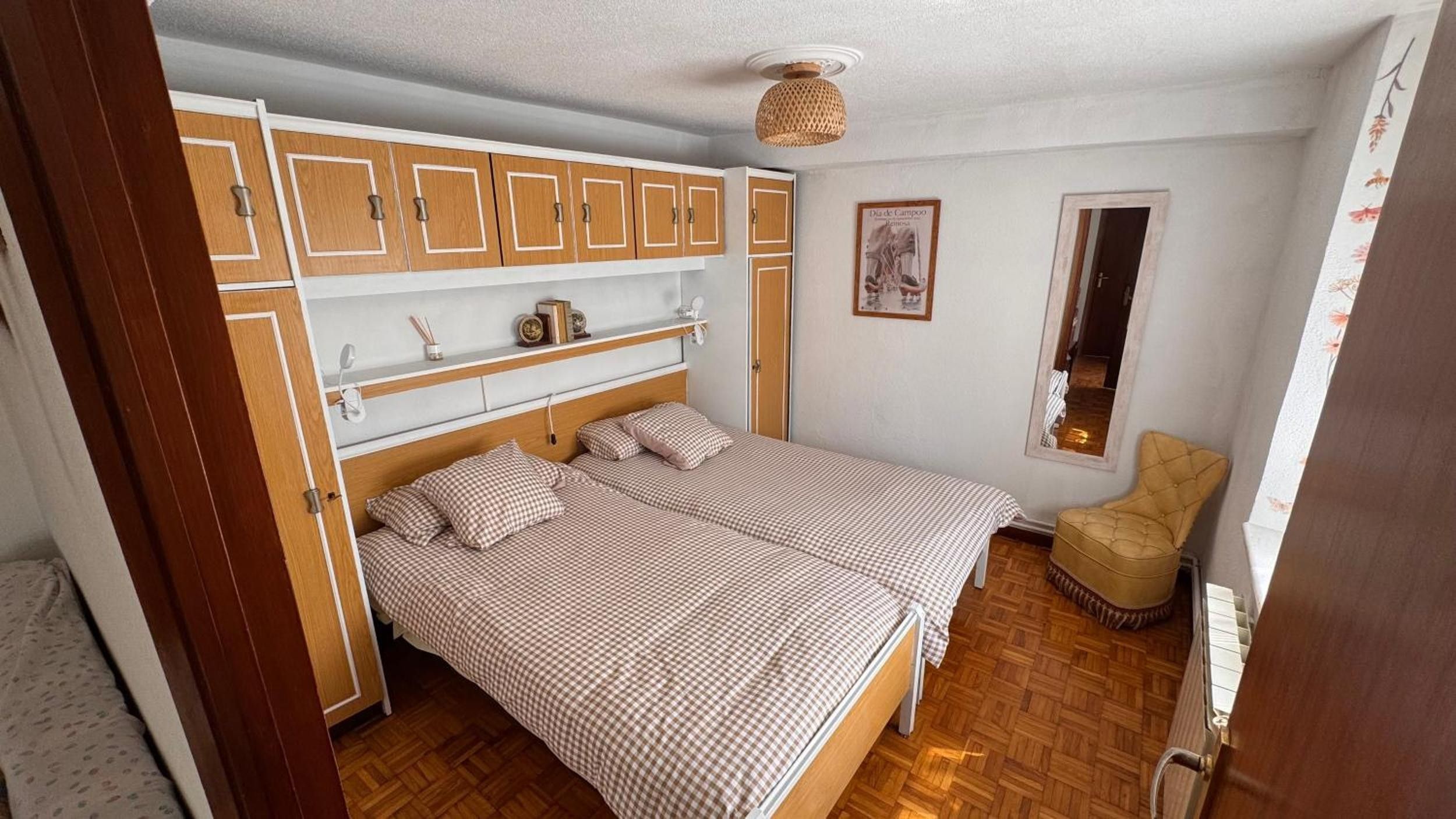Ein Schlafzimmer mit einem Bett, einem Holzschrank, Regalen, einem Stuhl und einem kleinen Fenster.
