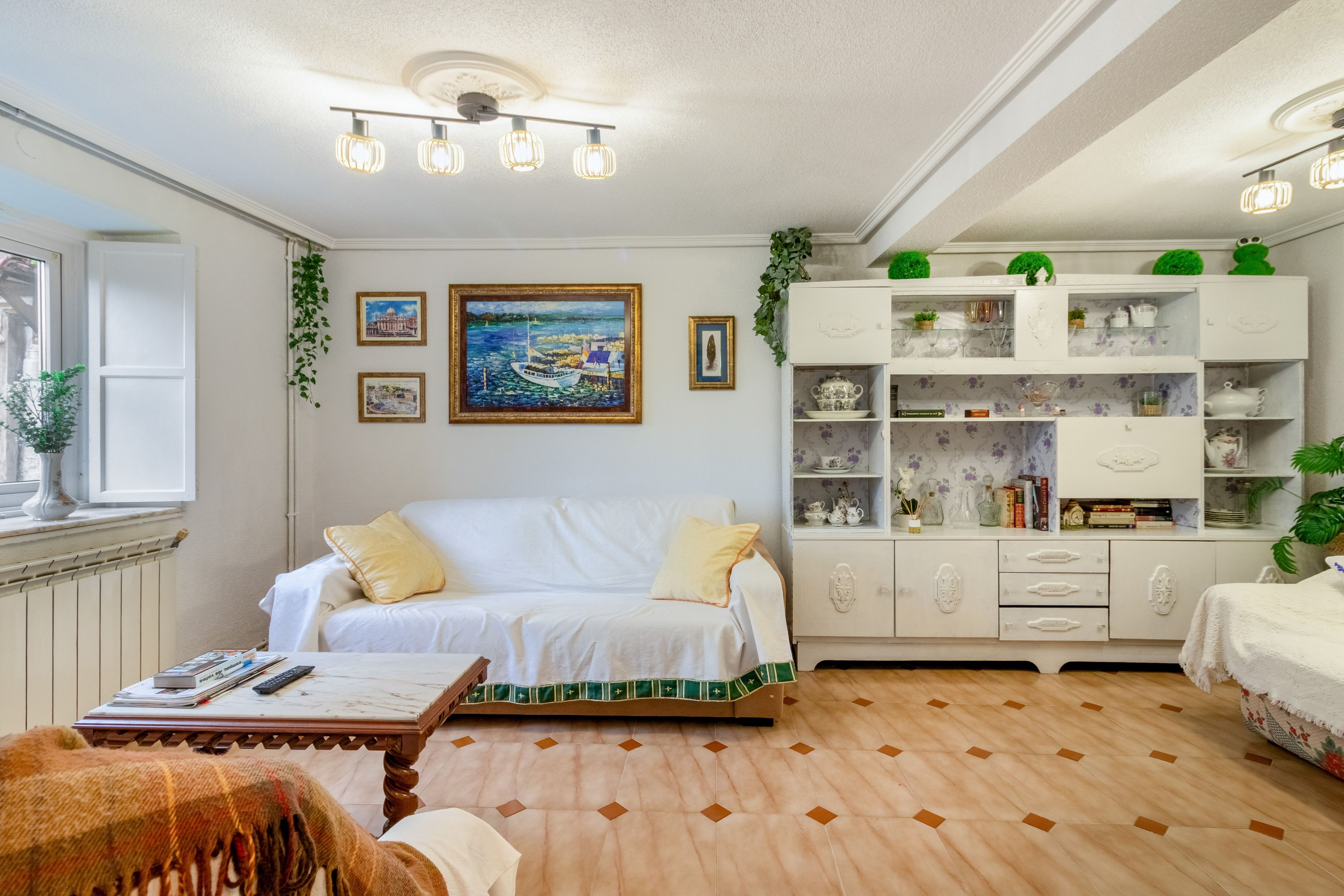 Een gezellige kamer met een witte bank, een houten salontafel en een boekenplank vol decoratieve objecten.