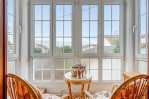 A room with a large window, a small table with a basket, and two wicker chairs.
