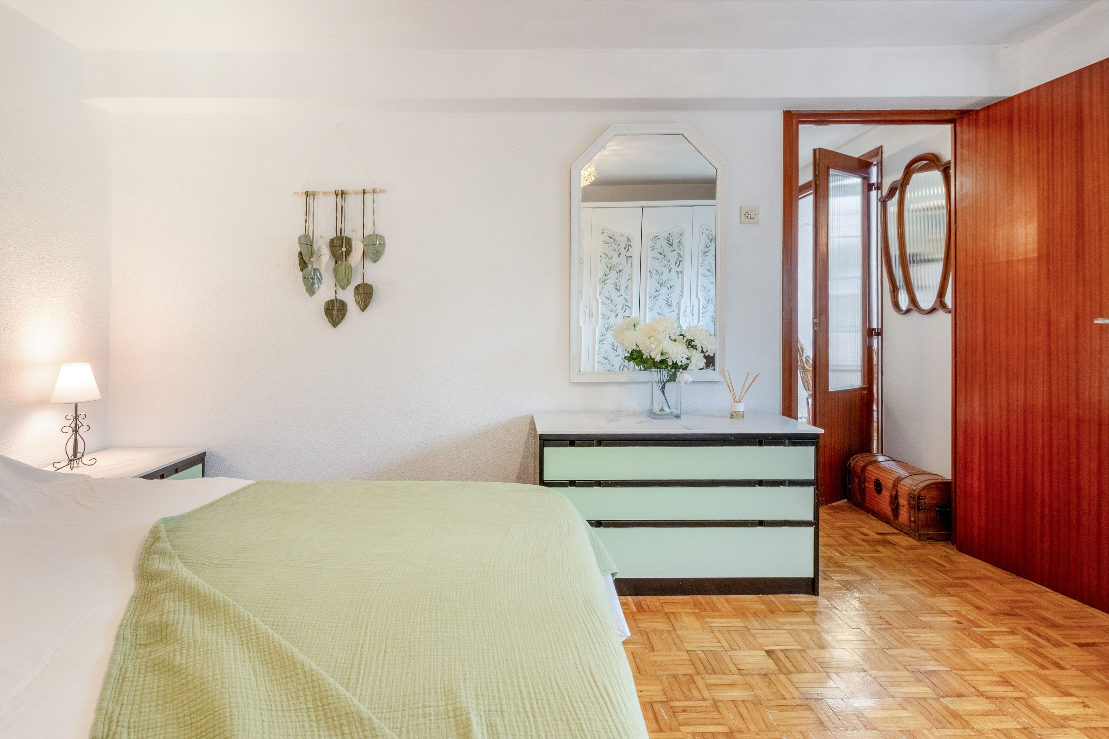 A bedroom with a bed, a dresser, a mirror, and a window with a view.