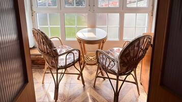 A room with a wooden herringbone floor, a round table with two chairs, and a view through a window with blinds.