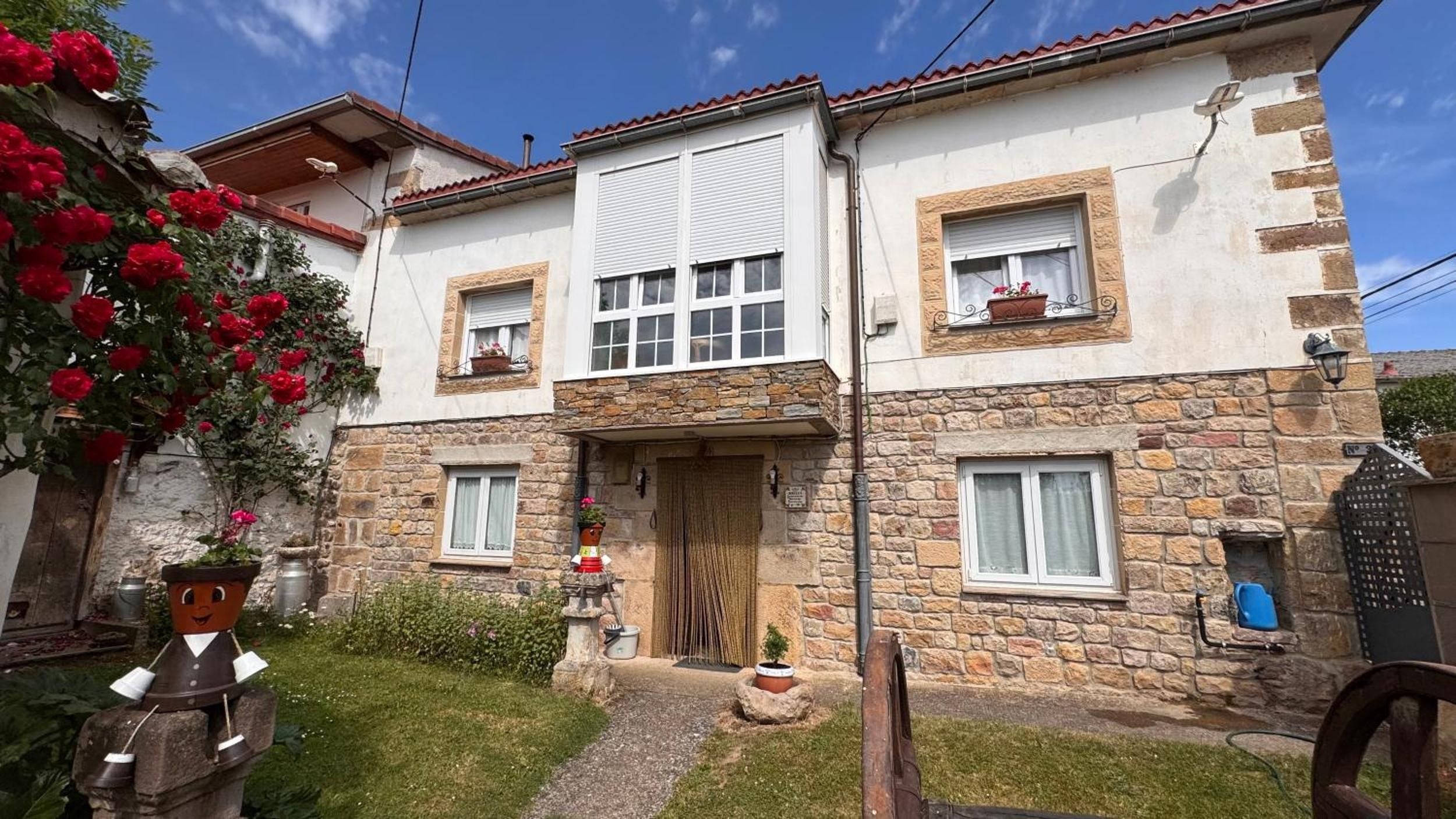 Une maison en pierre à deux étages, dotée d’une entrée centrale, d’un petit jardin et d’un espace extérieur de style rustique.