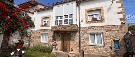 Une maison en pierre à deux étages, dotée d’une entrée centrale, d’un petit jardin et d’un espace extérieur de style rustique.