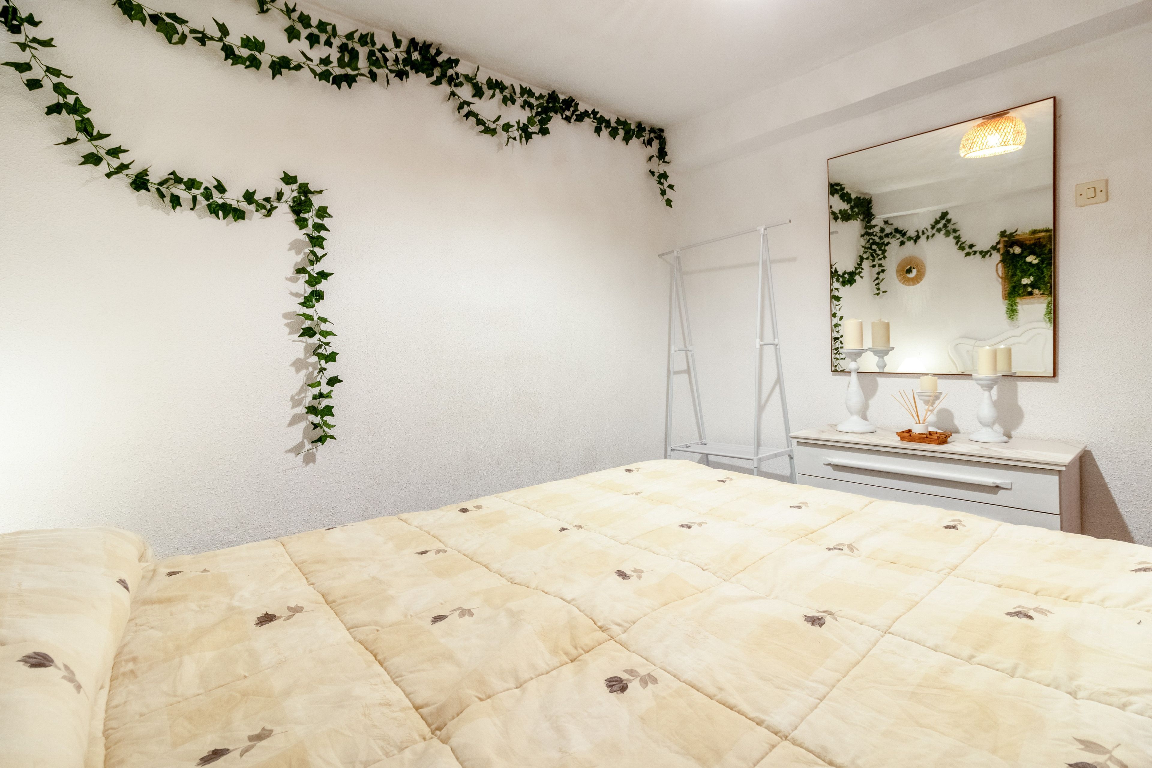 Een slaapkamer met een bed, een dressoir, een spiegel en decoratieve planten.