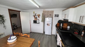 Eine kompakte Küche mit weißen Schränken, einer Mikrowelle, einem Kühlschrank und einem Esstisch mit Stühlen.