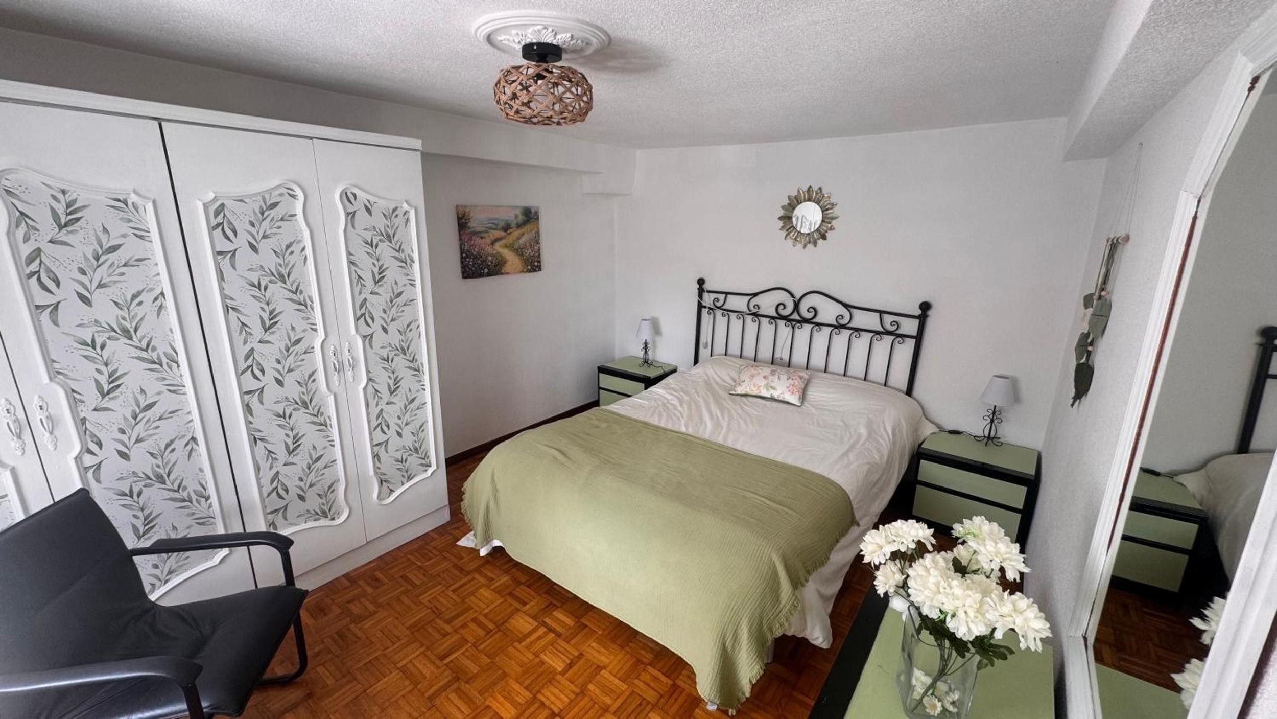 Een slaapkamer met een bed, nachtkastjes, een stoel, een kledingkast en een schilderij aan de muur.