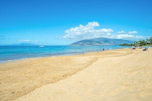 A wide sandy beach with clear blue water, a sailboat in the distance, and a mountain in the background. - Kihei Alii Kai C302 1 Bedroom Apts (Kihei)