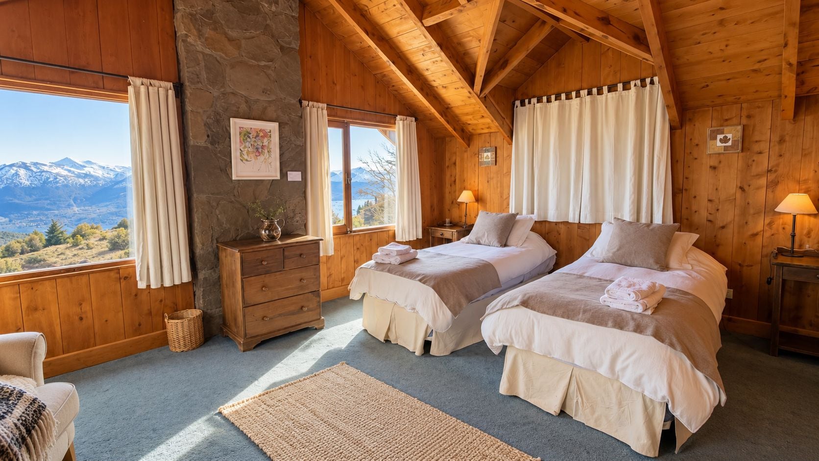 A cozy bedroom with two beds, a wooden dresser, a stone wall, and a view of mountains.