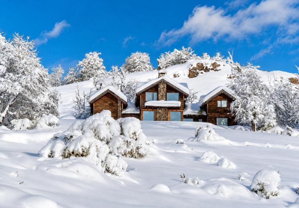 A snow-covered lodge with multiple cabins, surrounded by trees and a clear blue sky.