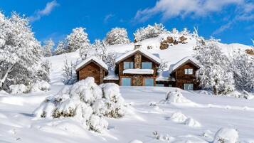 A snow-covered lodge with multiple cabins, surrounded by trees and a clear blue sky.