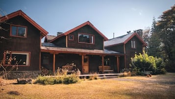 A two-story wooden house with a porch, a stone foundation, and a clear sky.