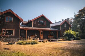 A two-story wooden house with a porch, a stone foundation, and a clear sky.