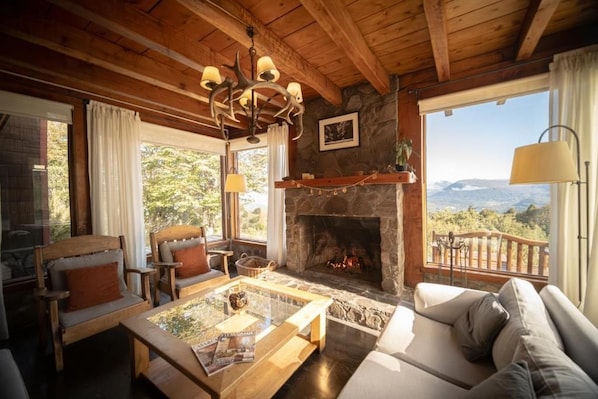 A cozy living room with a stone fireplace, wooden furniture, and a balcony with a view.