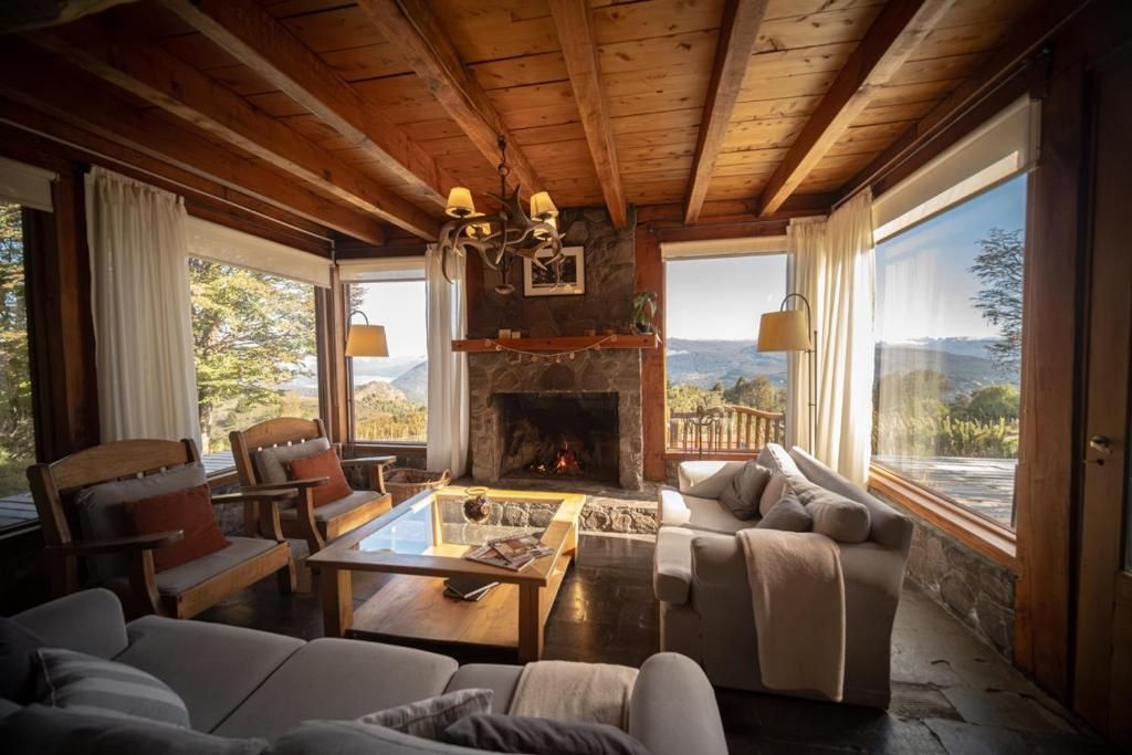 Una sala acogedora con chimenea, vigas de madera y ventanas amplias que ofrecen vistas a la montaña.