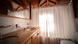 Un bagno in legno con un mobile contenitore in legno, due lavandini, uno specchio e un water.