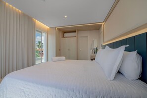Ein modernes Hotelzimmer mit einem großen Bett, einem Badezimmer mit Spiegel und Blick auf Palmen durch eine Schiebetür.