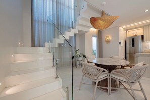 Ein modernes Interieur mit einer Glasstiege, einem runden Esstisch mit Korbstühlen und einer Küchenzeile inklusive Edelstahlkühlschrank.